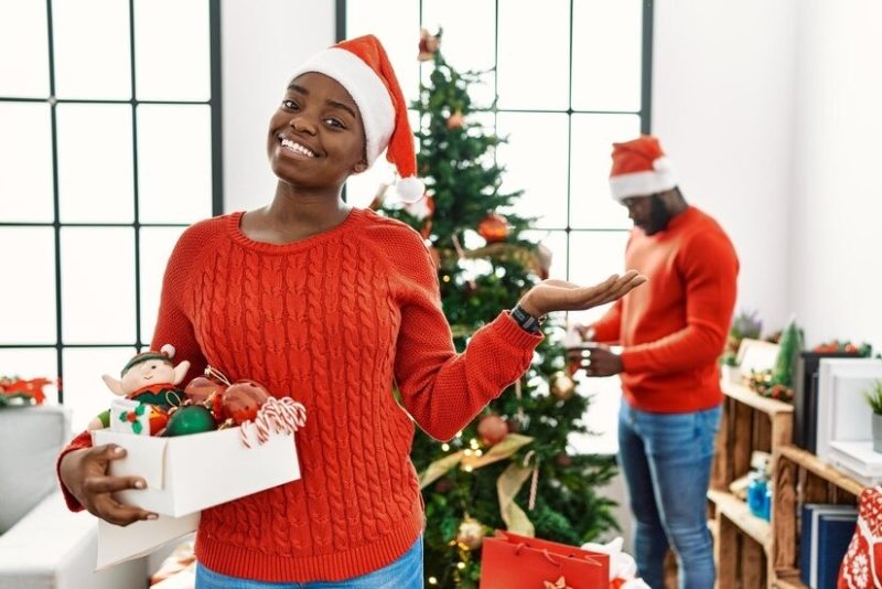 young-african-american-couple-standing-by-christmas-tree-smiling-cheerful-presenting-pointing-with-palm-hand-looking-camera_839833-32448-2